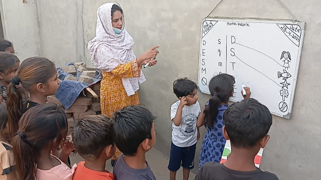 Excited children gather around the whiteboard as the teacher instructs them in reading.